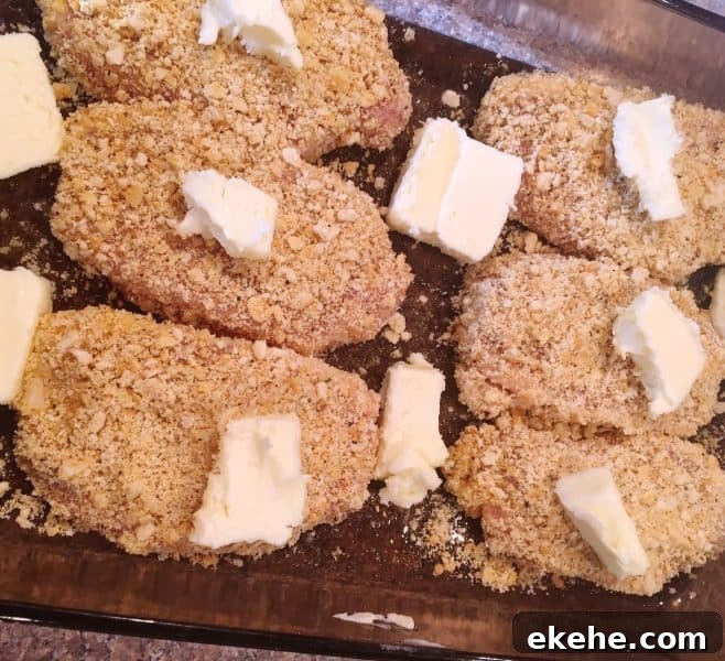 Breaded pork chops with dabs of butter on top and around them in a 9 x 13 baking pan.