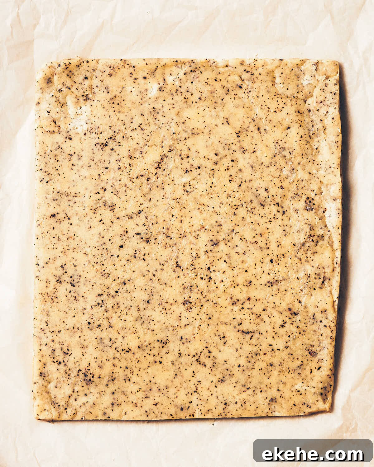 Earl grey shortbread dough that has been rolled into a square on parchment paper.
