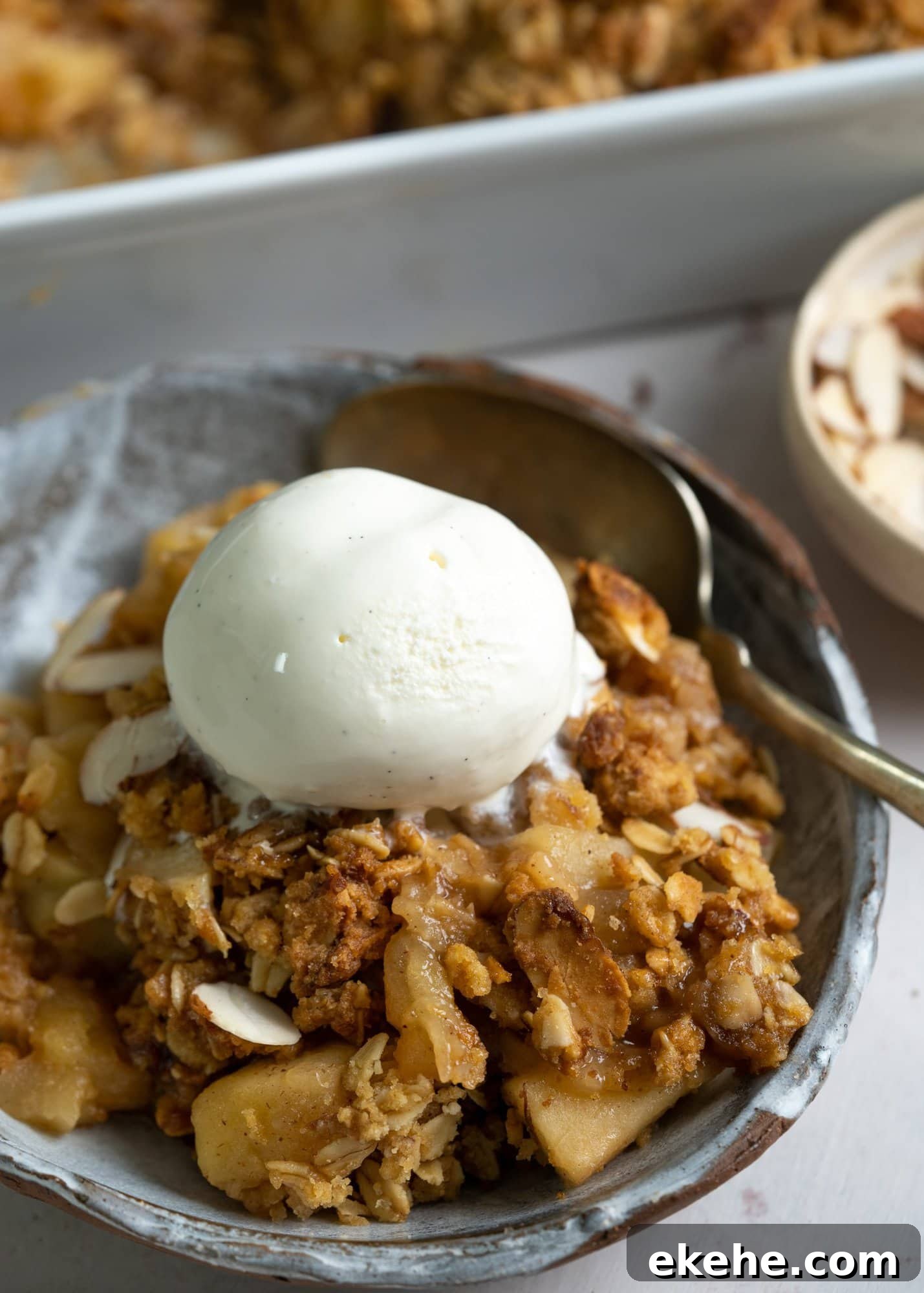 Apple crisp served on a bowl with a scoop of vanilla ice cream on top and spoon.