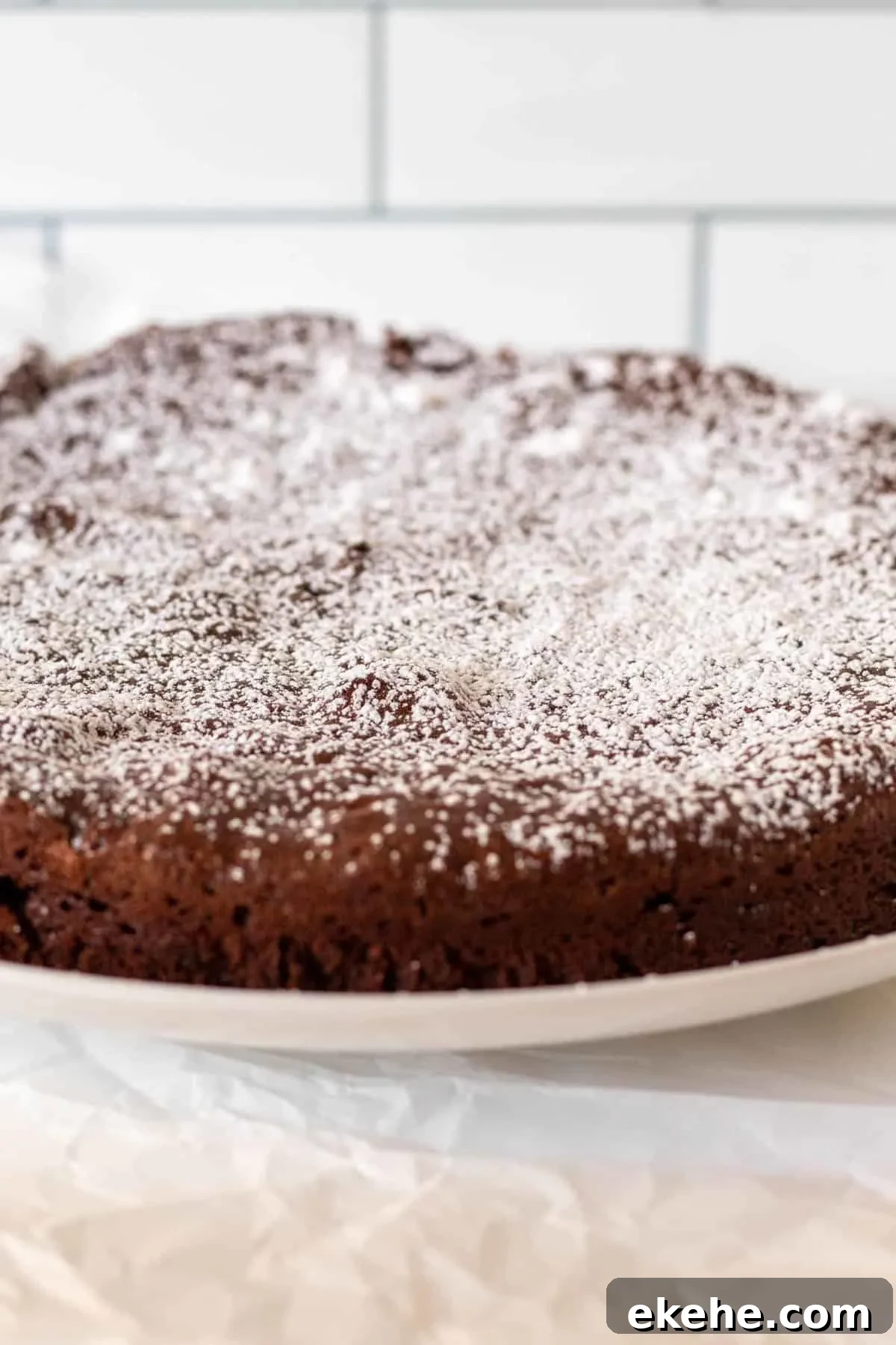 Whole bittersweet cake on white plate dusted with powdered sugar.