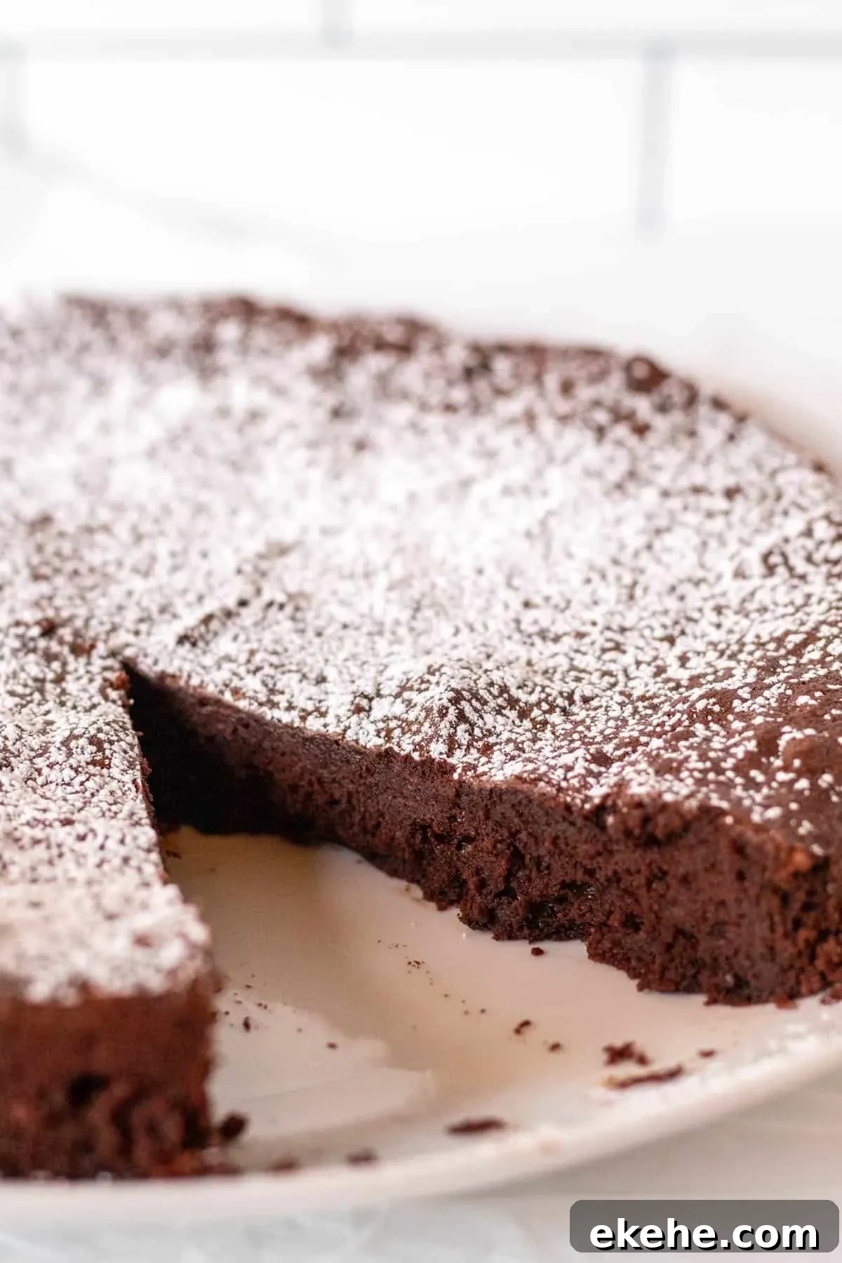 Whole bitterswweet chocolate cake with powdered sugarr and pice cut out.