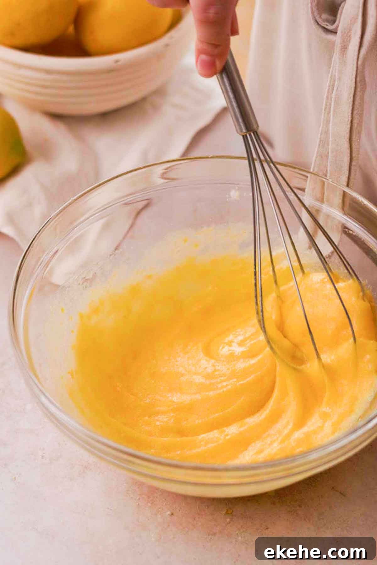 whisking eggs sugar and lemon zest in a glass bowl with a wire whisk