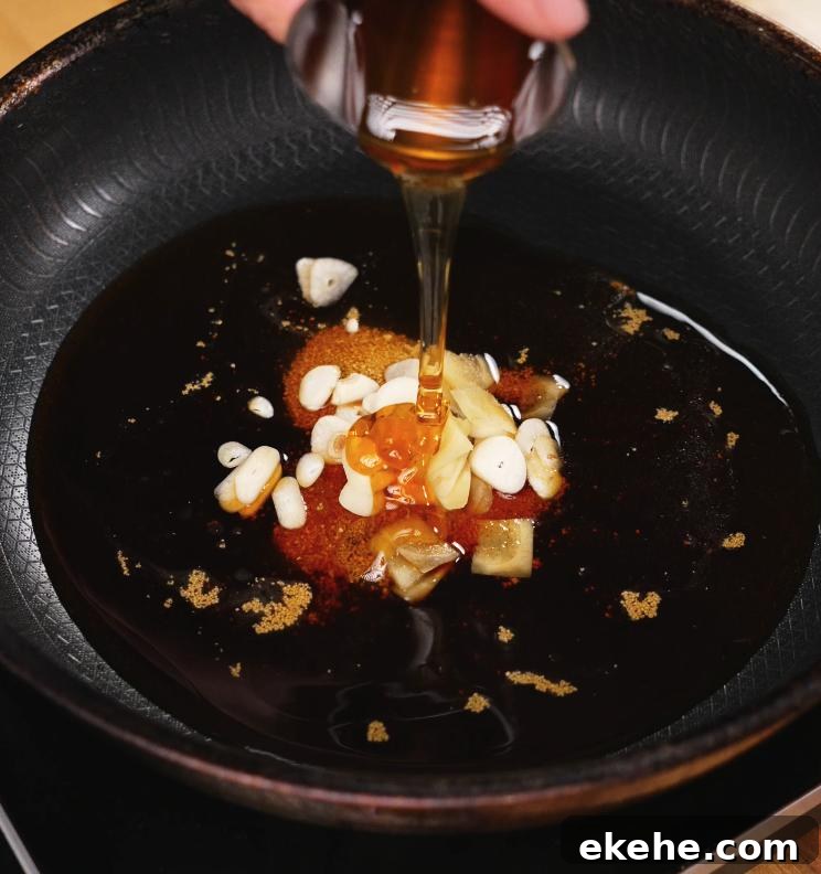 A glass container of honey is being poured into a pan containing garlic, ginger, and soy sauce, forming the rich and aromatic braising base for the chicken.