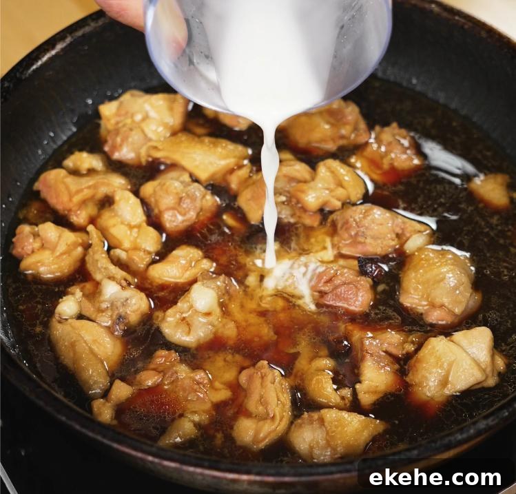 A cornstarch slurry is being poured into the simmering ginger soy chicken mixture, helping thicken the sauce to a glossy finish.