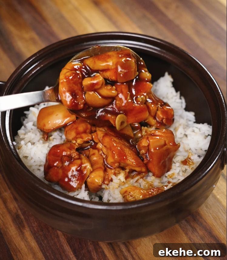 A spoonful of glossy, thick ginger braised chicken is being drizzled over a fresh bowl of steamed white rice, showcasing the final serving step.