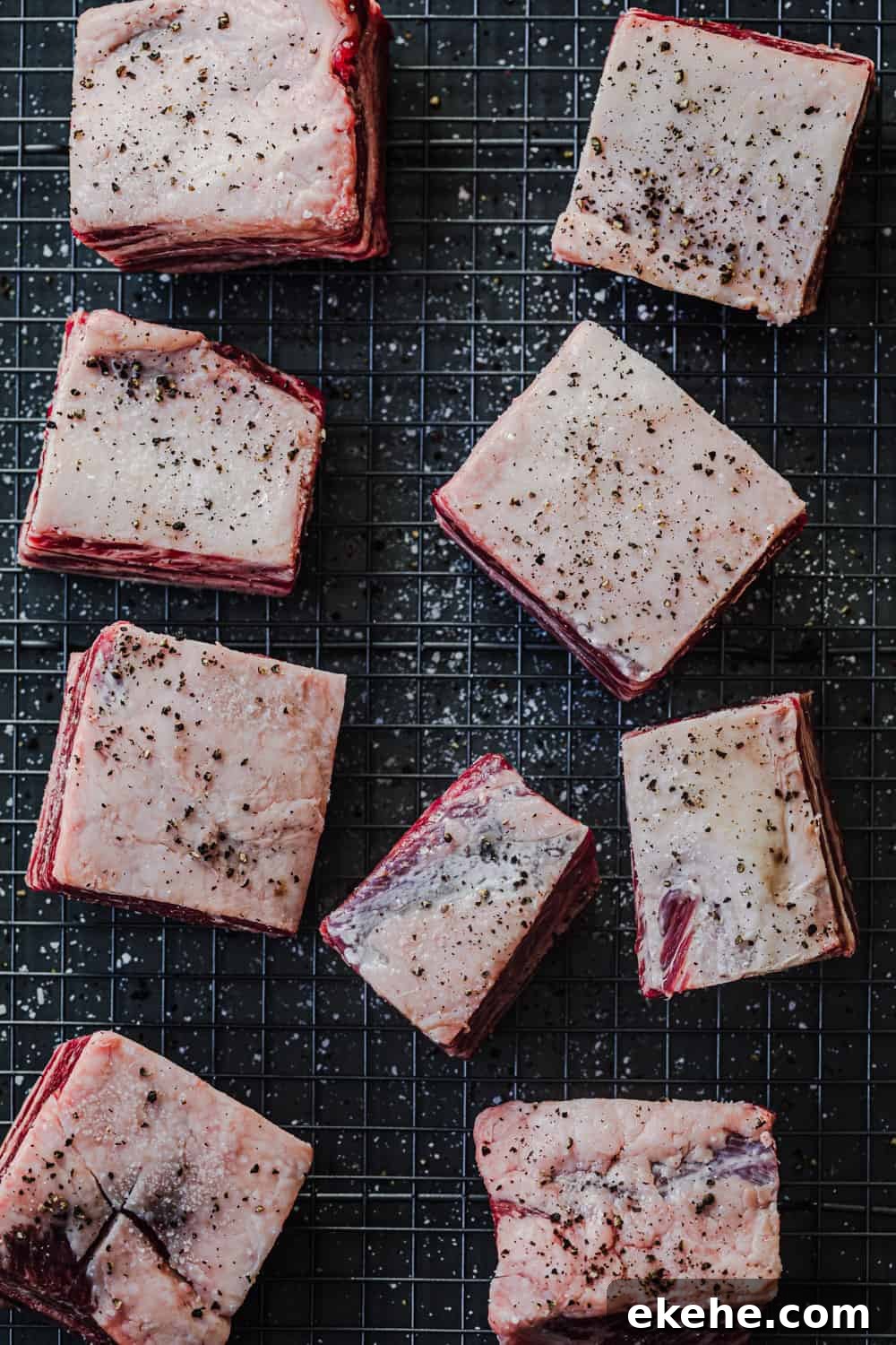 ingredient shot: raw short ribs, seasoned with salt and pepper, on a wire rack on a baking tray.