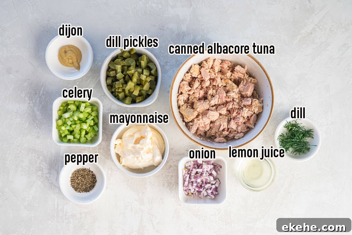 Ingredients for dill pickle tuna salad arranged in small bowls, including albacore tuna, dill pickles, mayonnaise, celery, red onion, Dijon mustard, fresh dill, lemon juice, and black pepper.
