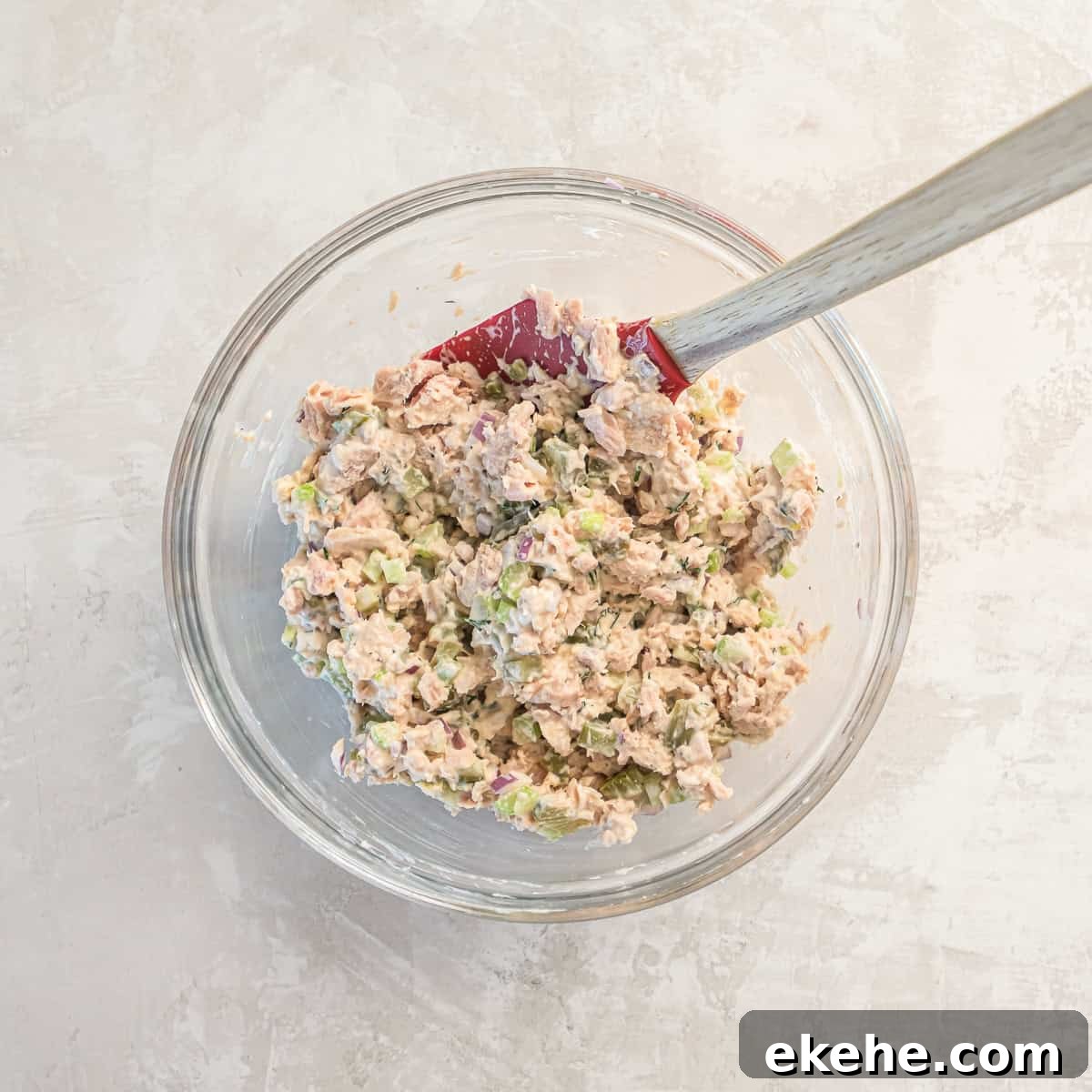 Dill pickle tuna salad fully mixed in a glass bowl with a spatula.