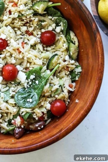 orzo greek pasta salad in large wooden bowl with lemons in another bowl