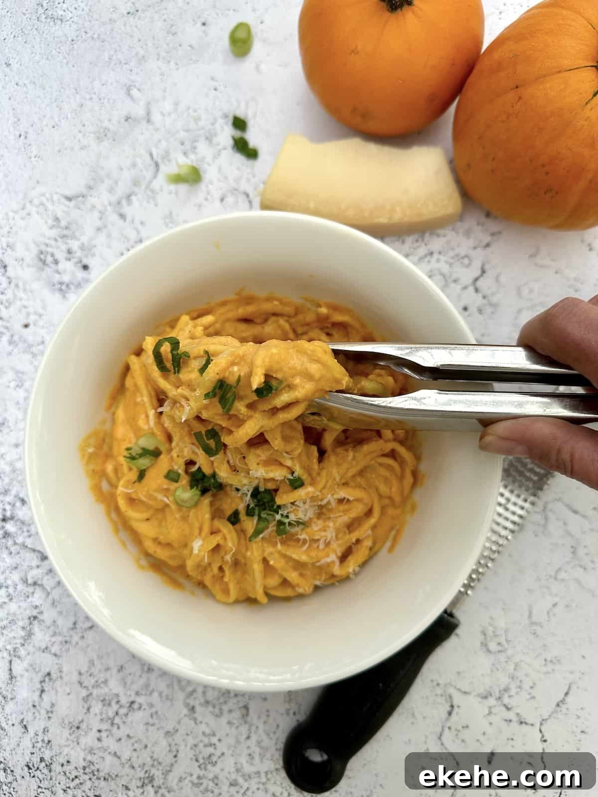 Pumpkin sauce with pasta in a bowl with pumkins and a wedge of parmesan cheese on the side.