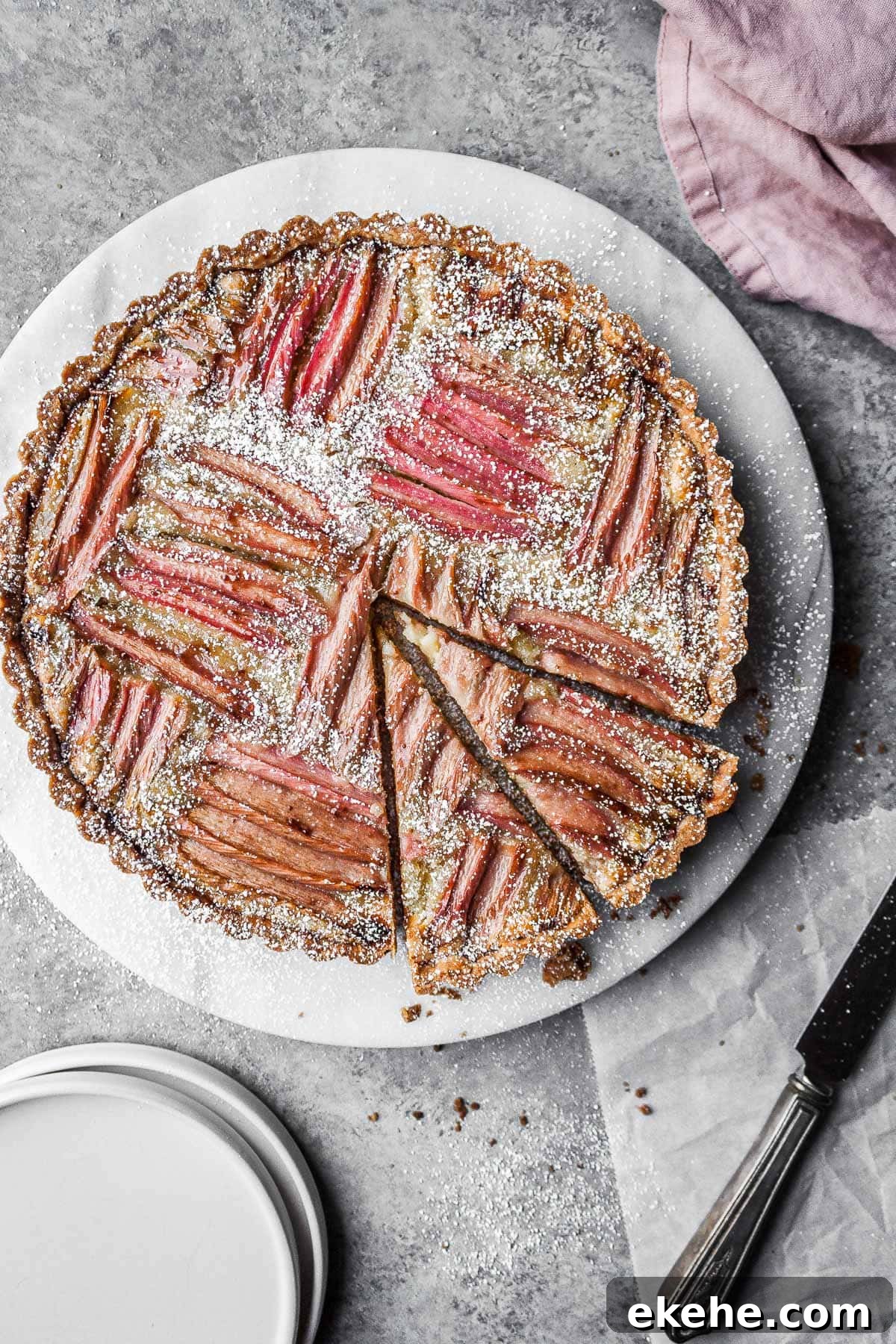 Rhubarb frangipane tart on a round marble platter with two slices cut.
