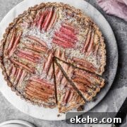 Rhubarb frangipane tart on a round marble platter with two slices cut.