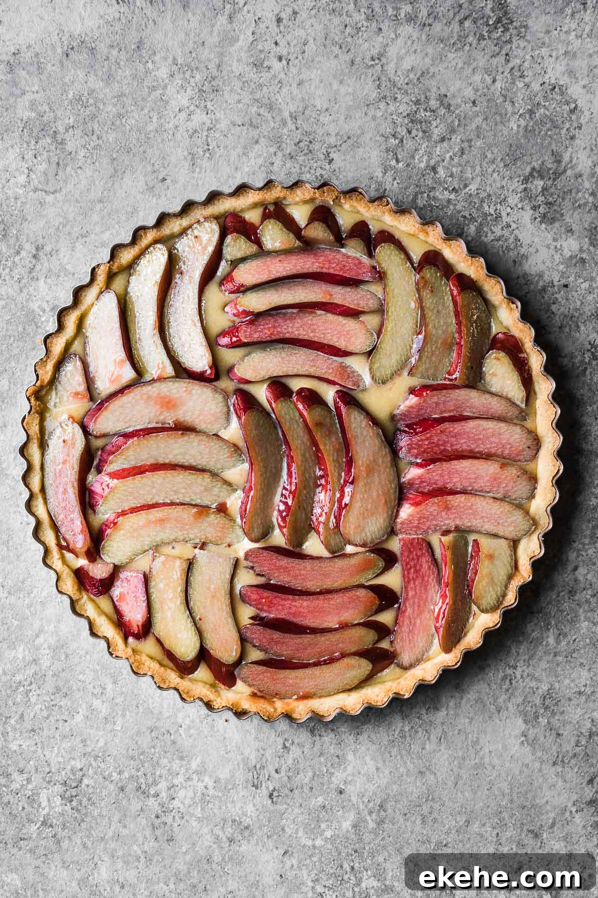 Unbaked tart filled with frangipane and topped with sliced rhubarb arranged in a parquet pattern.