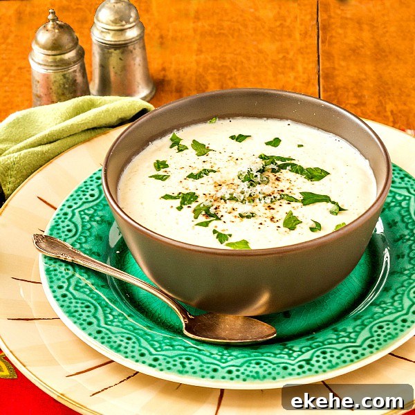 A bowl of cream of cauliflower soup on a green plate with chopped herbs for garnish.