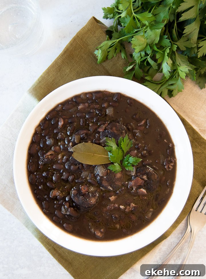 A white bowl holds Brazilian Black Beans, garnished with parsley and a bay leaf