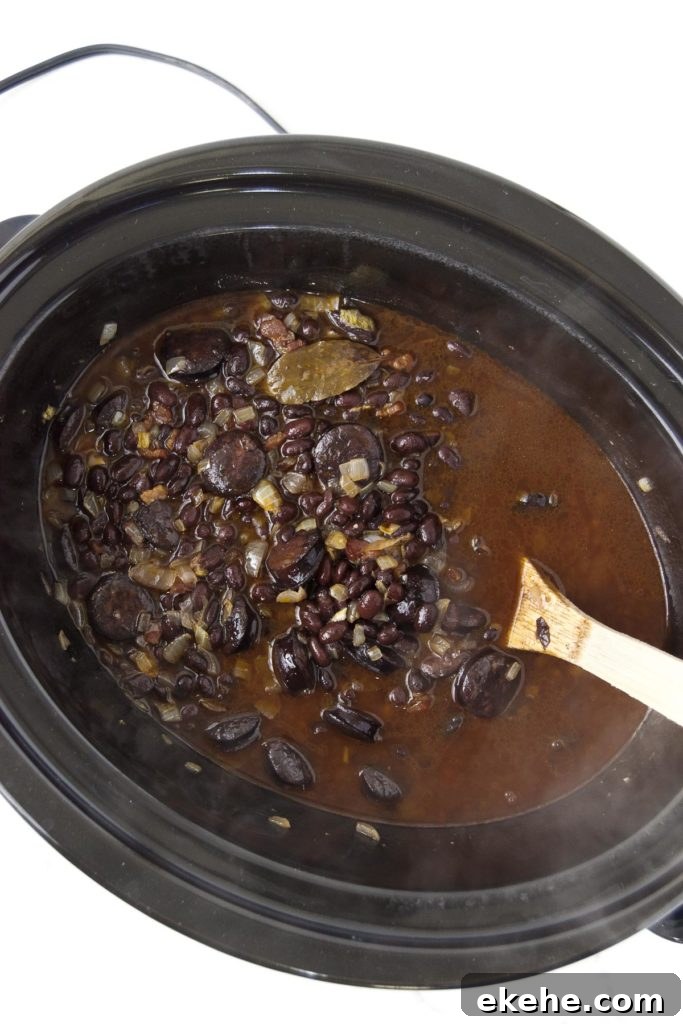 The final slow cooker black beans in a slow cooker being stirred with a wooden spoon
