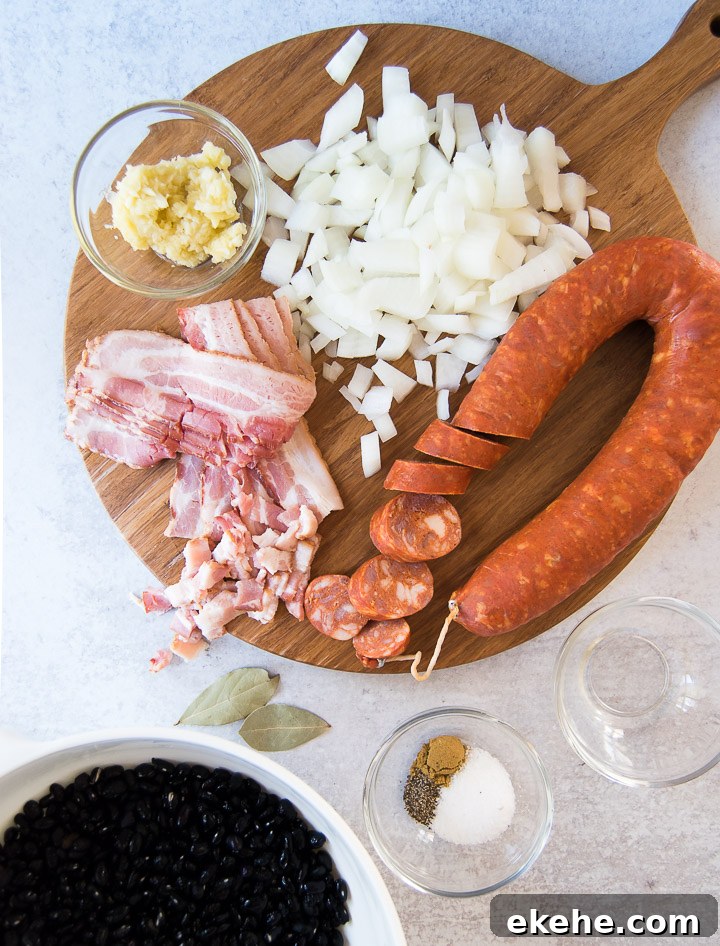 A wooden cutting board holds a sausage, bacon, sofrito and onion next to a bowl of black beans