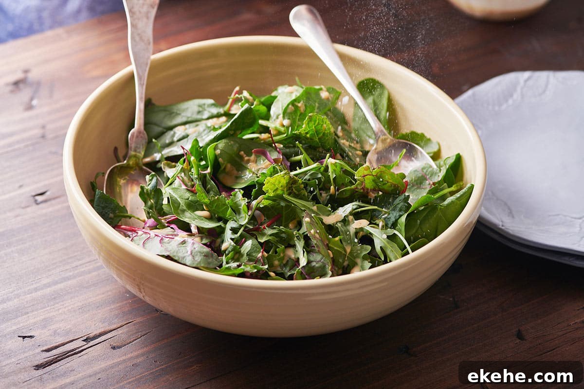 Mixed Green Salad with Creamy Sesame Dressing in brown serving bowl on table with spoons.