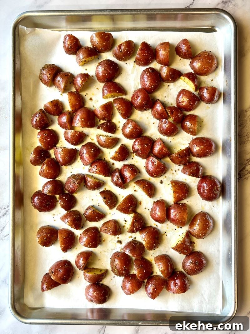 Seasoned halved potatoes in a single layer on a large sheet pan lined with parchment paper.
