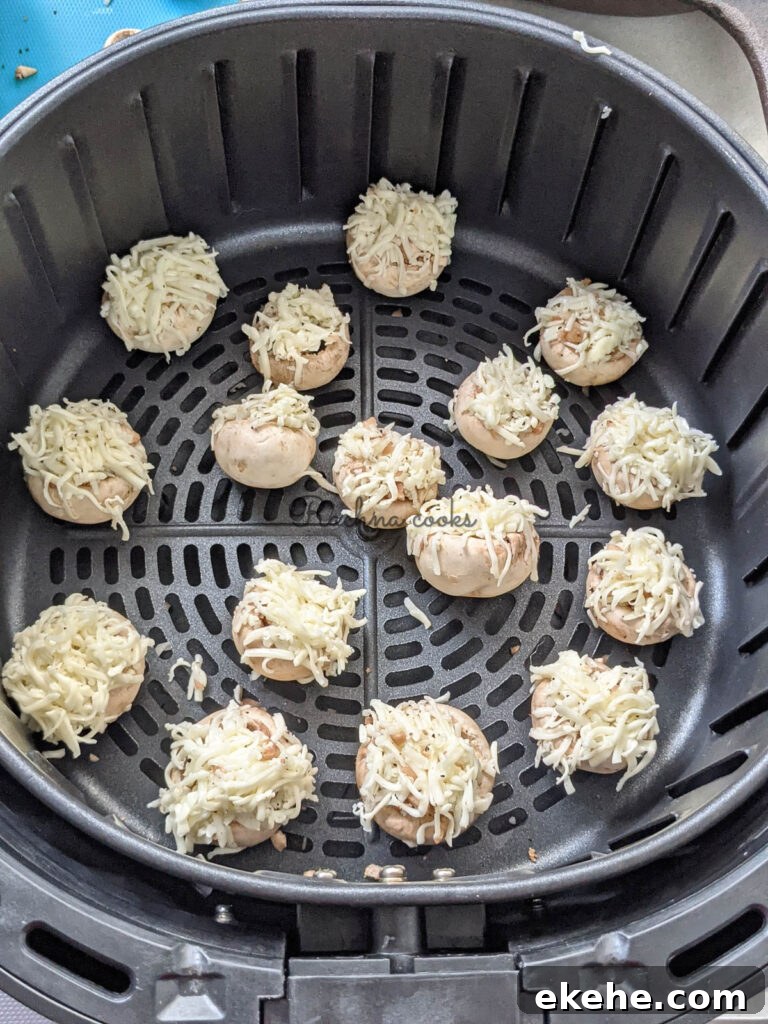 Mushroom caps stuffed and garnished with grated cheese ready for air frying in air fryer basket.