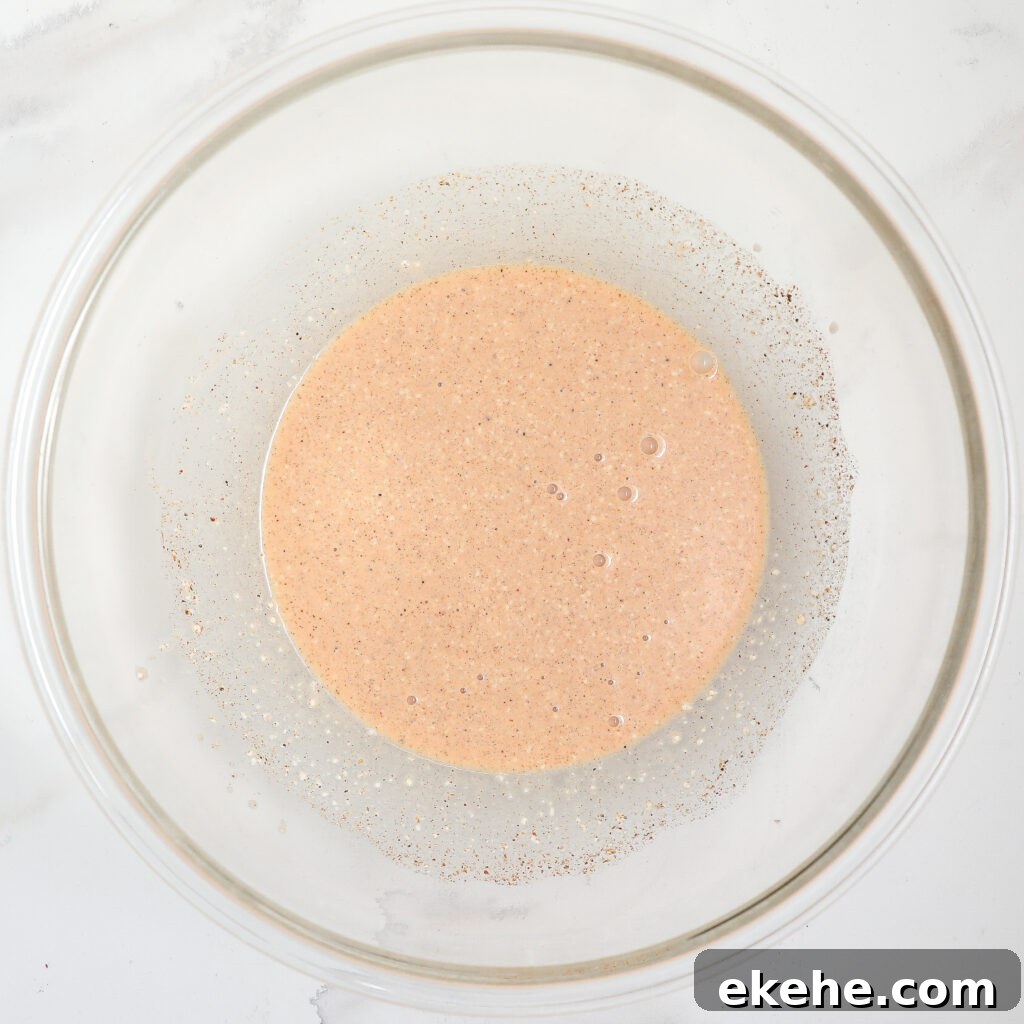 A glass mixing bowl containing a light brown, slightly frothy liquid batter sits on a white surface, ready for baking—perfect to pair with a fresh corn and avocado salad with bacon.