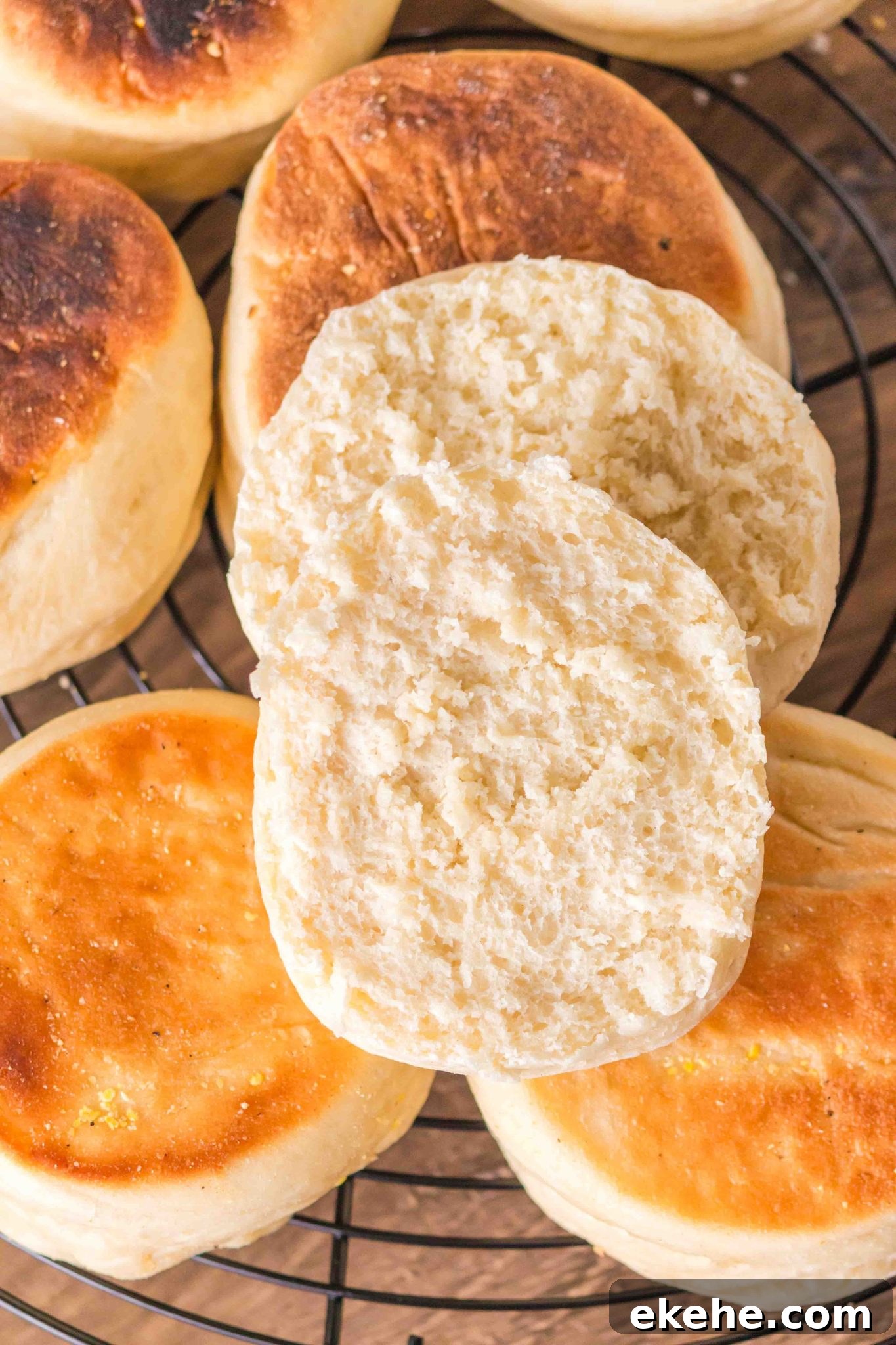 Golden brown english muffins sitting on a cooling rack with the top one cut in half - Hostess At Heart
