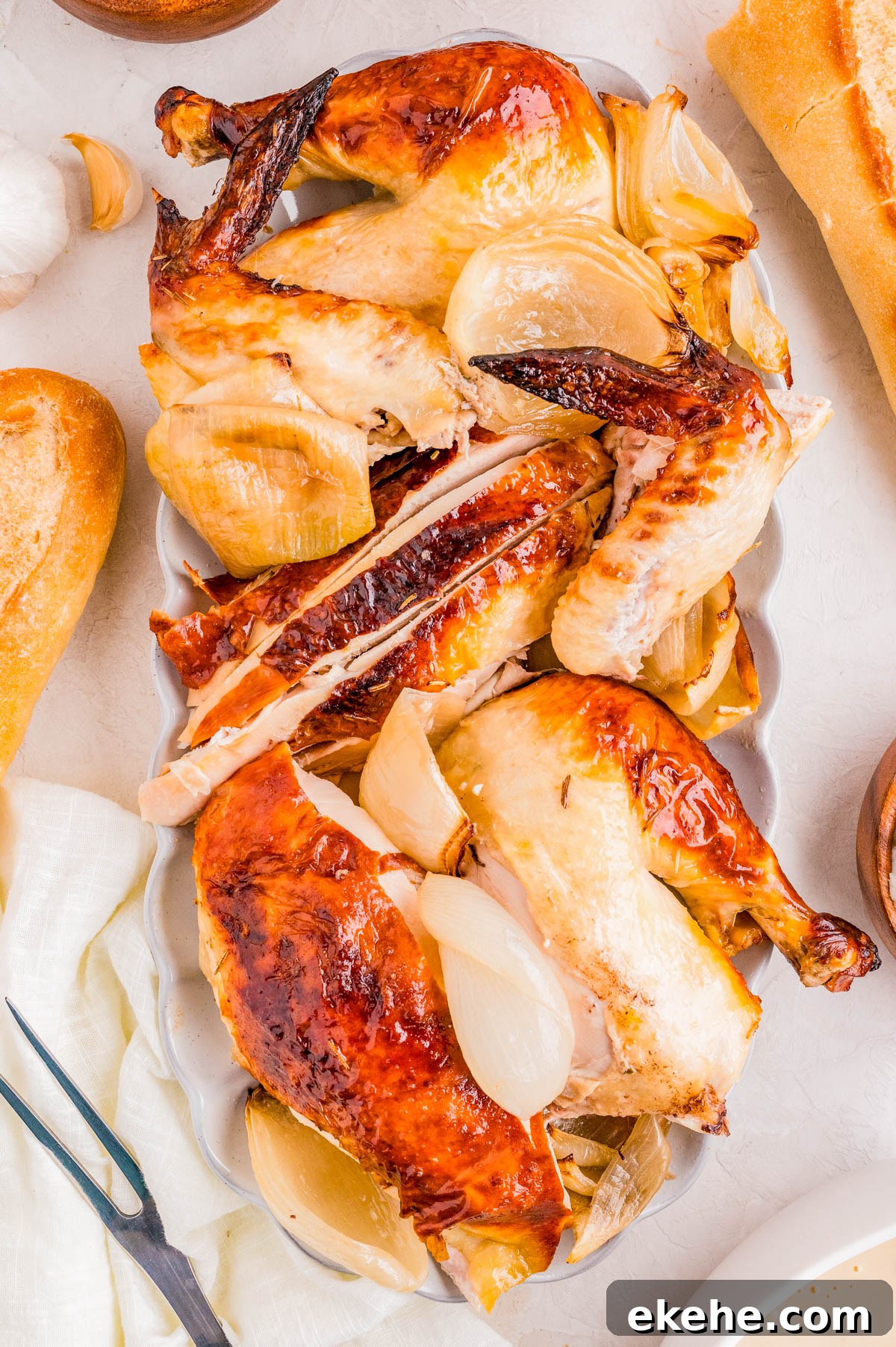 Roast chicken cut into pieces and served with roasted onions on a white platter, surrounded by bread and utensils.