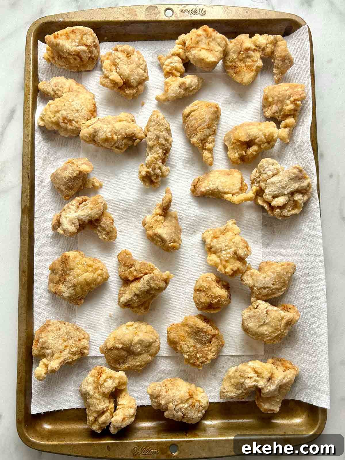 fried pork pieces resting on paper towel-lined baking sheet.