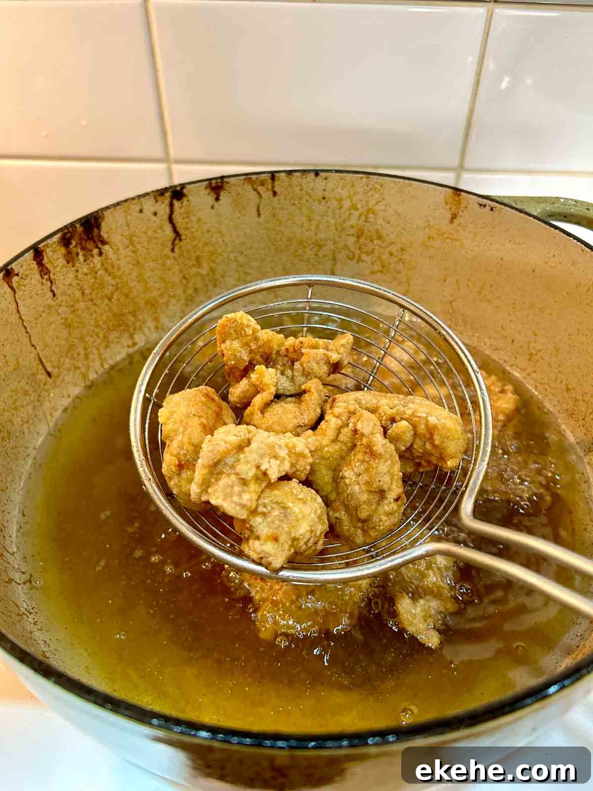 double-fried pork pieces being lifted out of oil with metal spider.