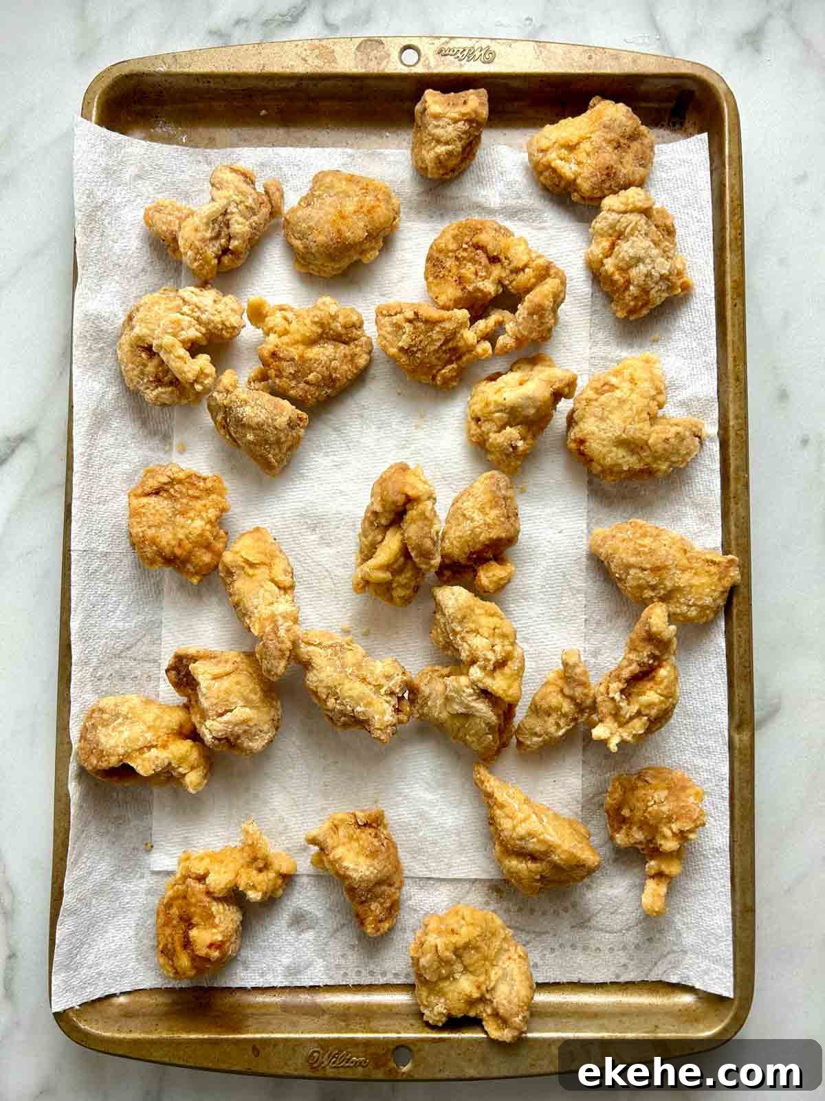 double-fried fried pork pieces resting on paper towel-lined baking sheet.