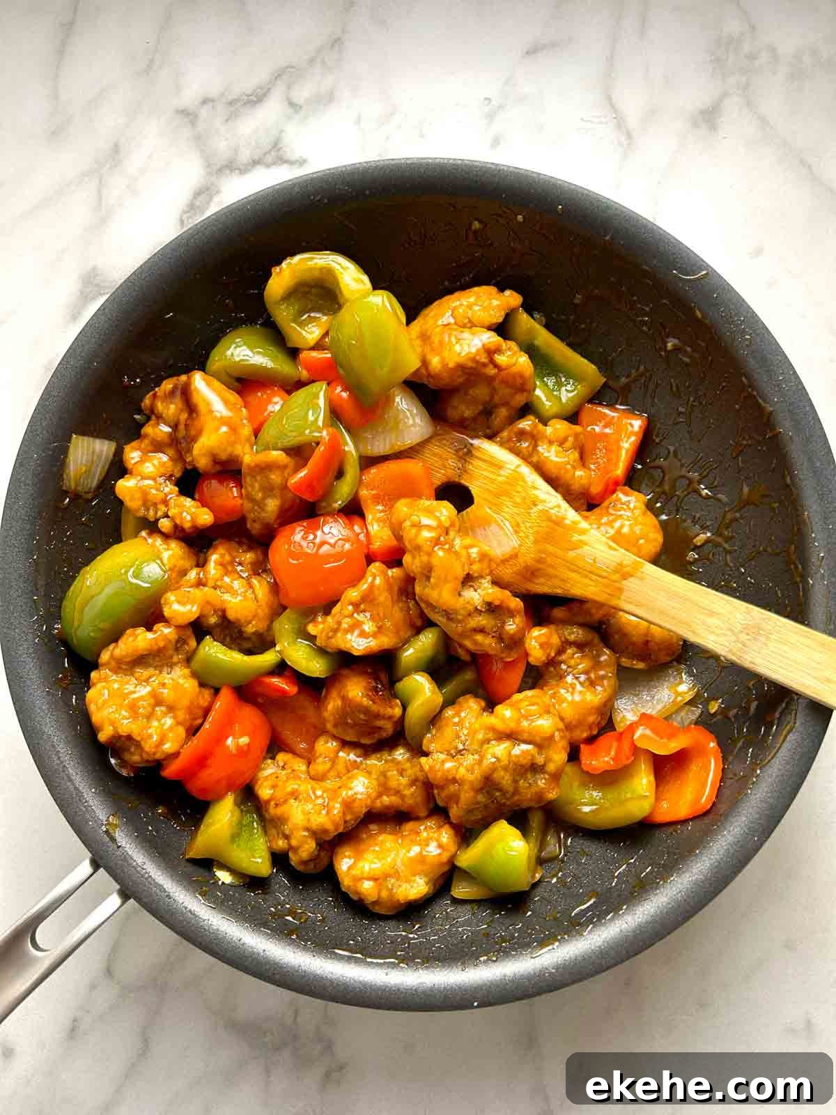 sauce being mixed with fried pork in pan.