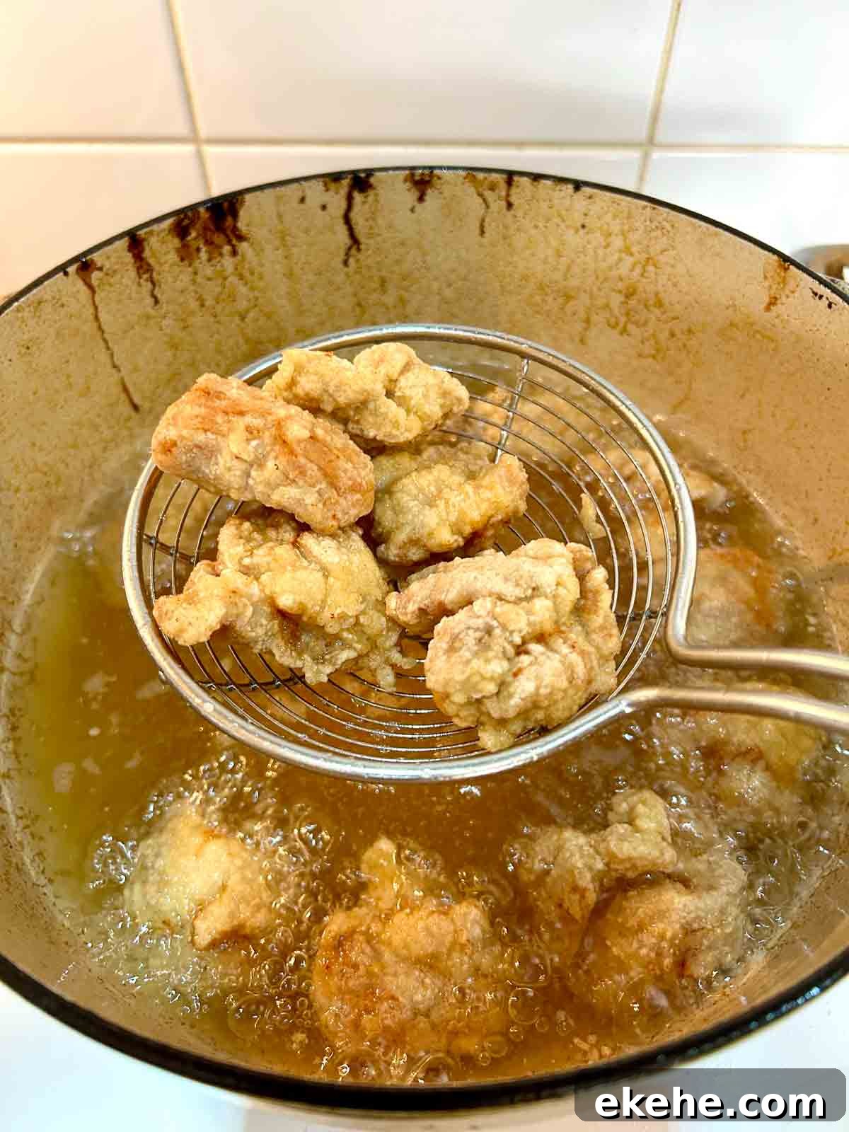 fried pork pieces being lifted out of oil with metal spider.