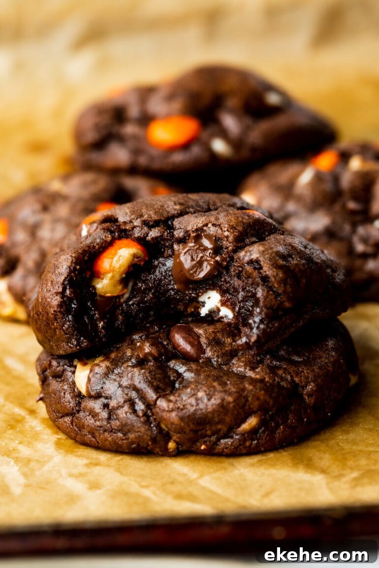 a photo of thick and chewy triple chocolate cookies one stacked on top of another and bite taken out of the top cookie