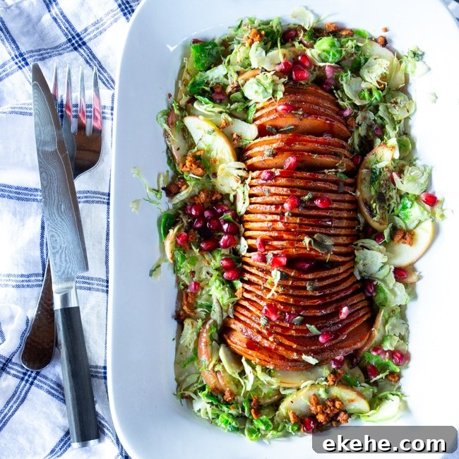 A large platter of thinly sliced, pomegranate-glazed butternut squash, surrounded by a Brussels sprouts and apple salad.