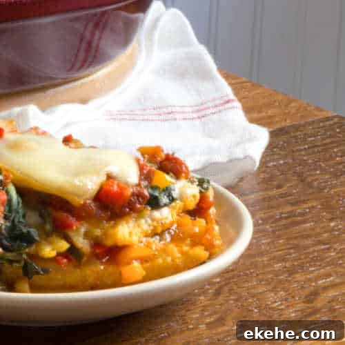 Cheesy polenta lasagna on a plate, layered with peppers, spinach and tomato sauce.