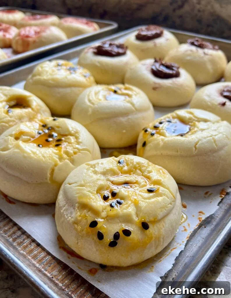 Freshly baked sourdough kolaches with jam centers cooling on a parchment-lined baking sheet.