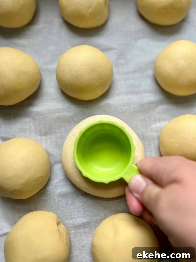 Pressing indentations into sourdough kolache dough rounds with the bottom of a measuring cup before adding filling.
