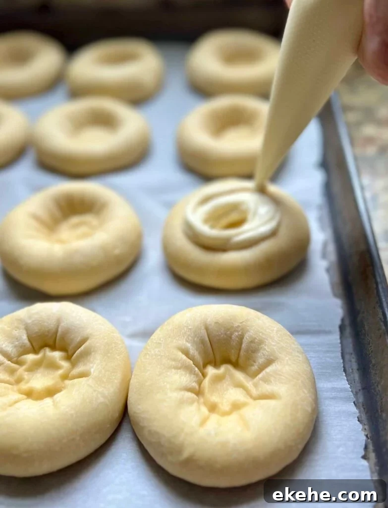 Piping cream cheese filling into sourdough kolache dough rounds.