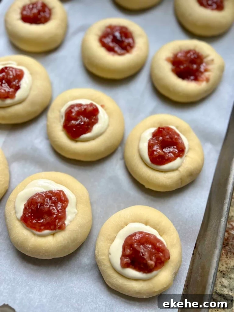 Sourdough kolaches filled with fruit jam and cream cheese filling on a baking sheet before baking.
