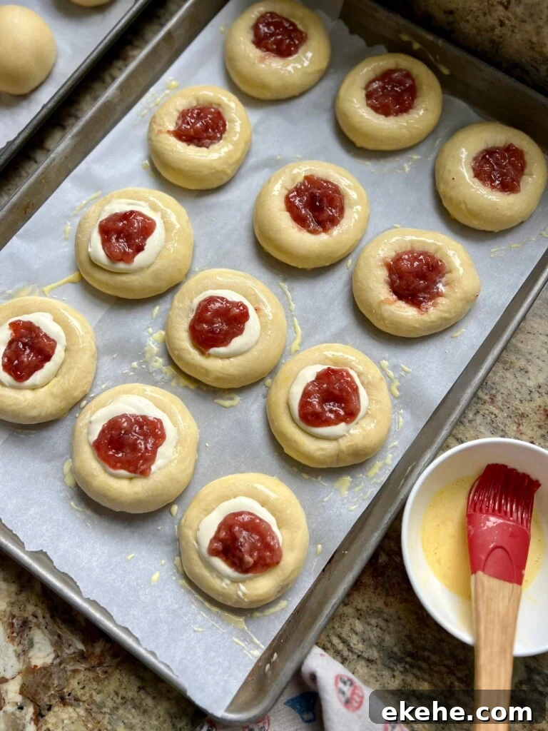 Tray of unbaked sourdough kolaches with cream cheese and fruit jam filling ready for the oven.