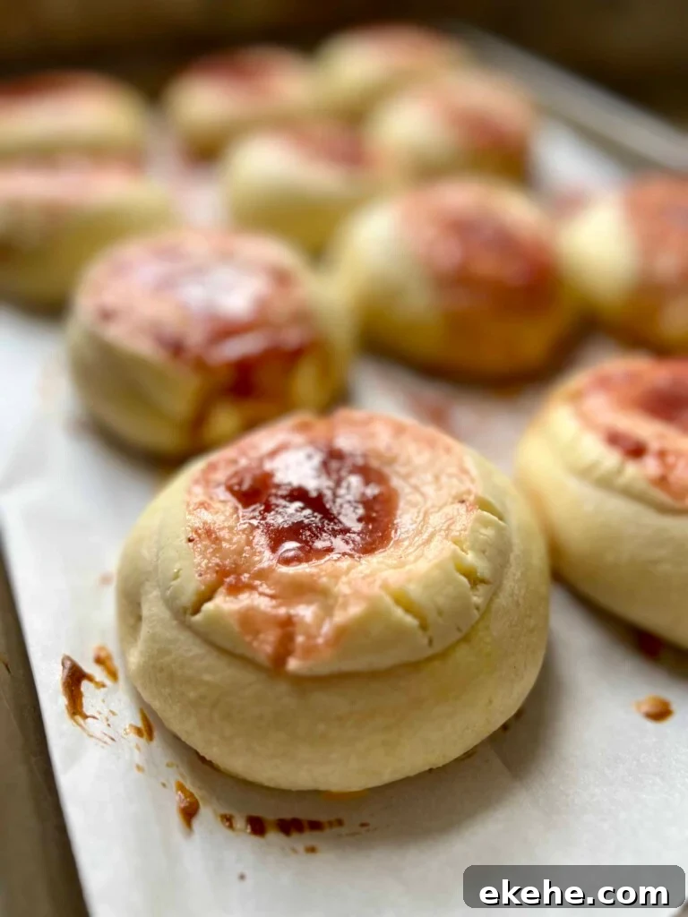 Freshly baked sourdough kolaches with fruit jam centers cooling on a parchment-lined baking sheet.