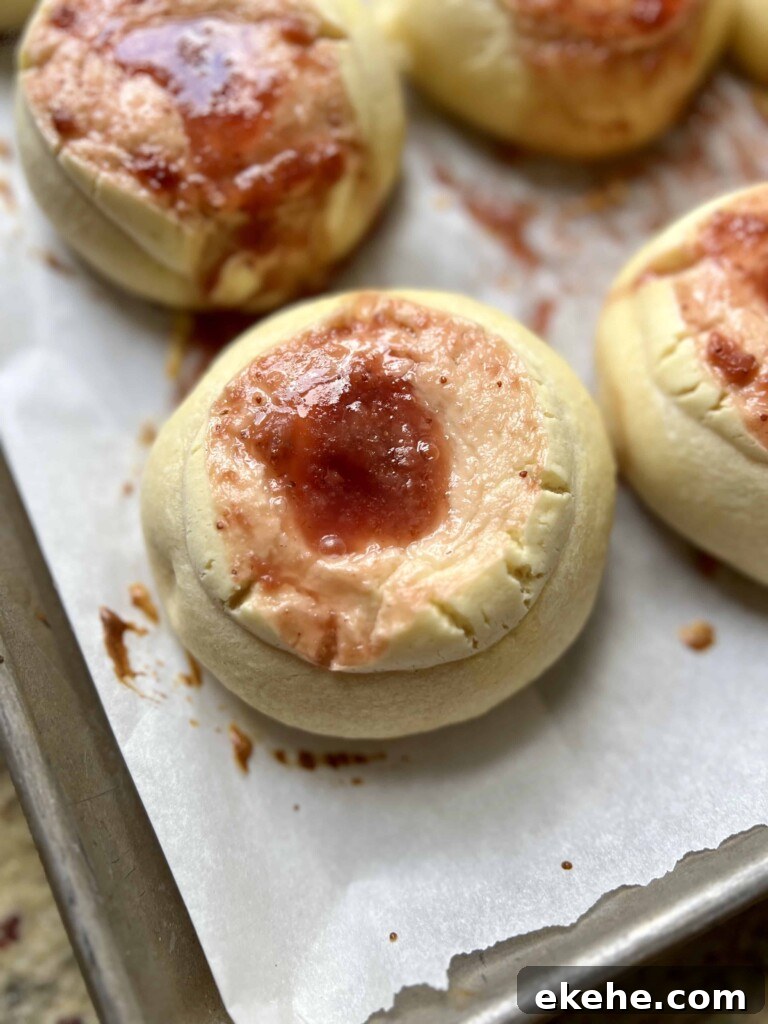 Golden brown sourdough kolaches with fruit filling baked on parchment paper.