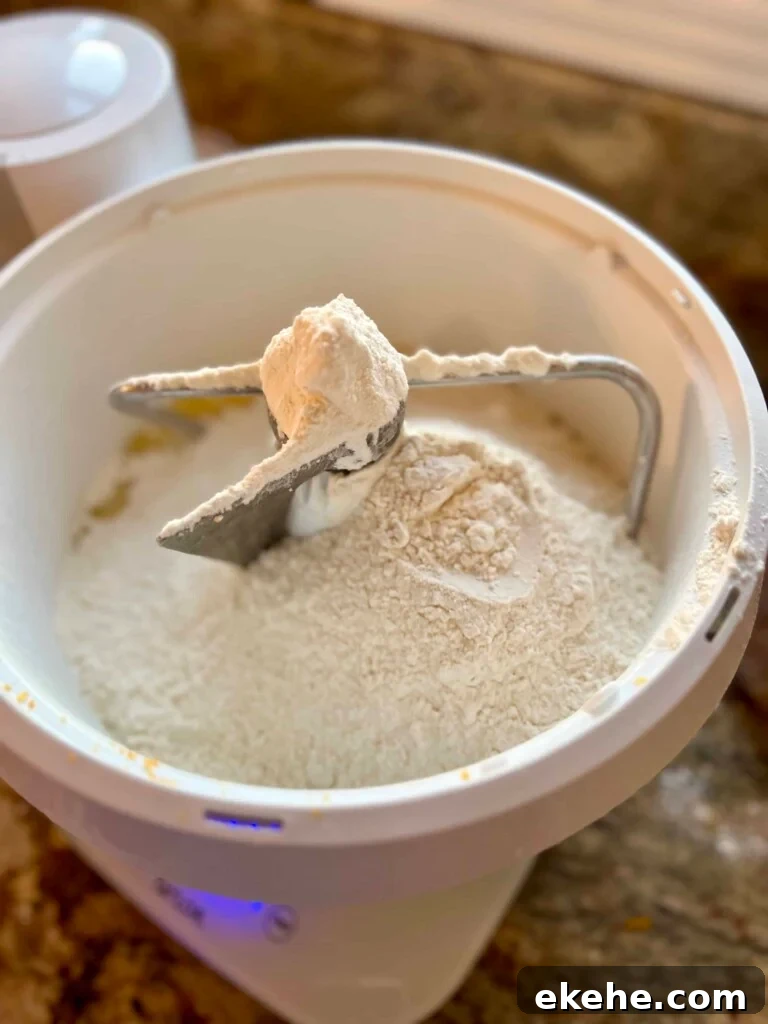 Flour and ingredients for sourdough kolache dough sitting in the bowl of a mixer.
