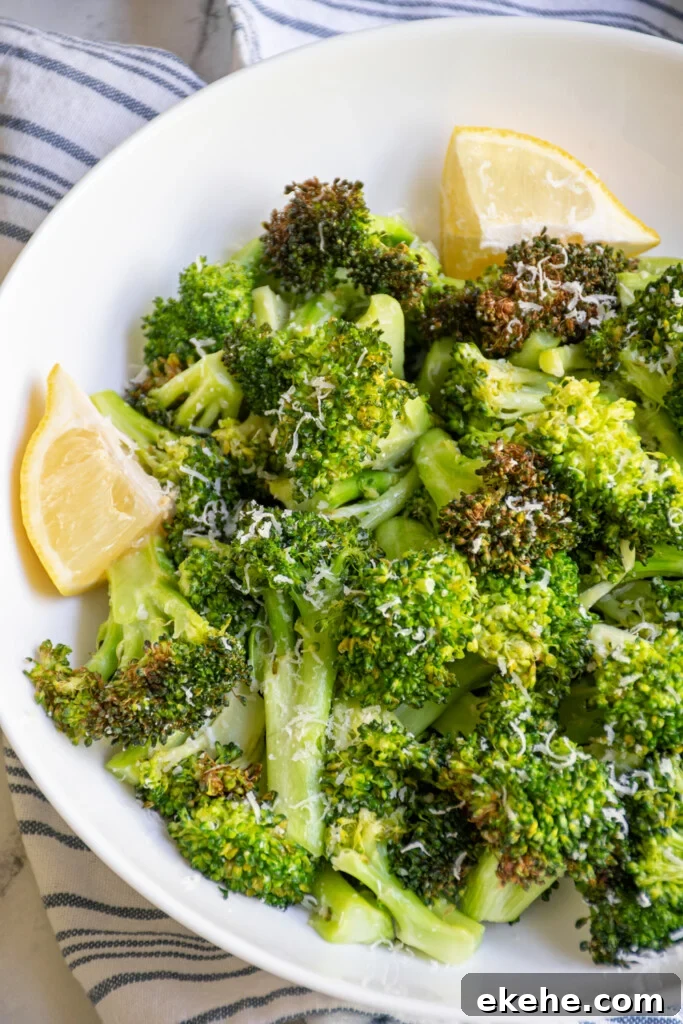 A white bowl filled with air fryer broccoli garnished with parmesan cheese and lemon wedges.