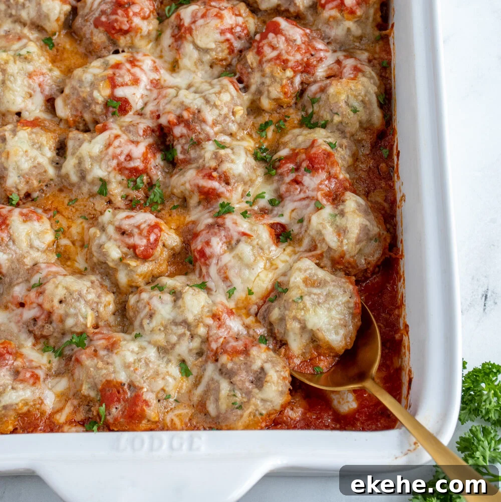 White casserole dish with baked turkey meatballs in sauce covered with cheese and fresh parsley.