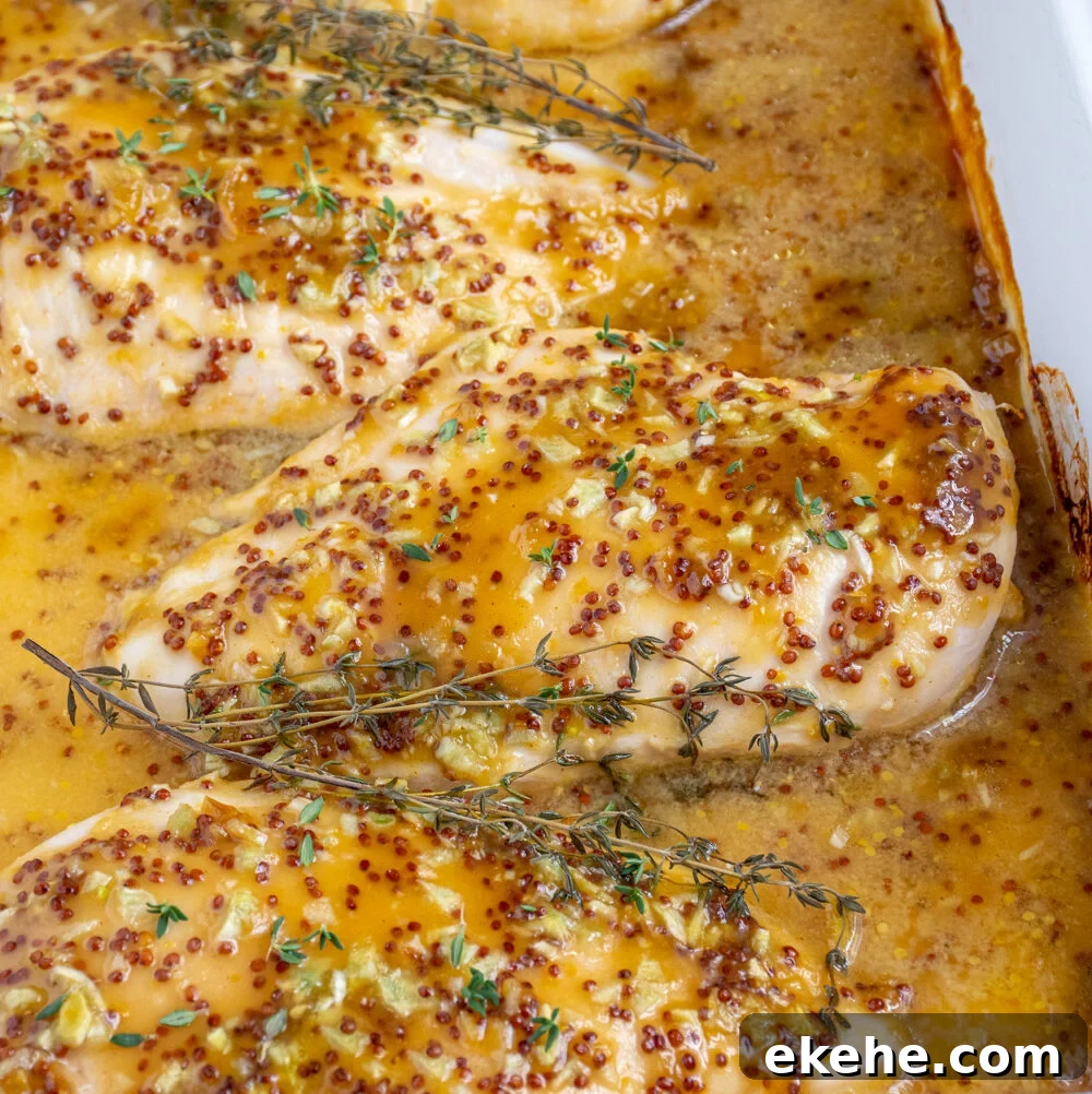 Baked Honey Mustard Chicken in a casserole dish covered in homemade sauce and garnished with fresh thyme.