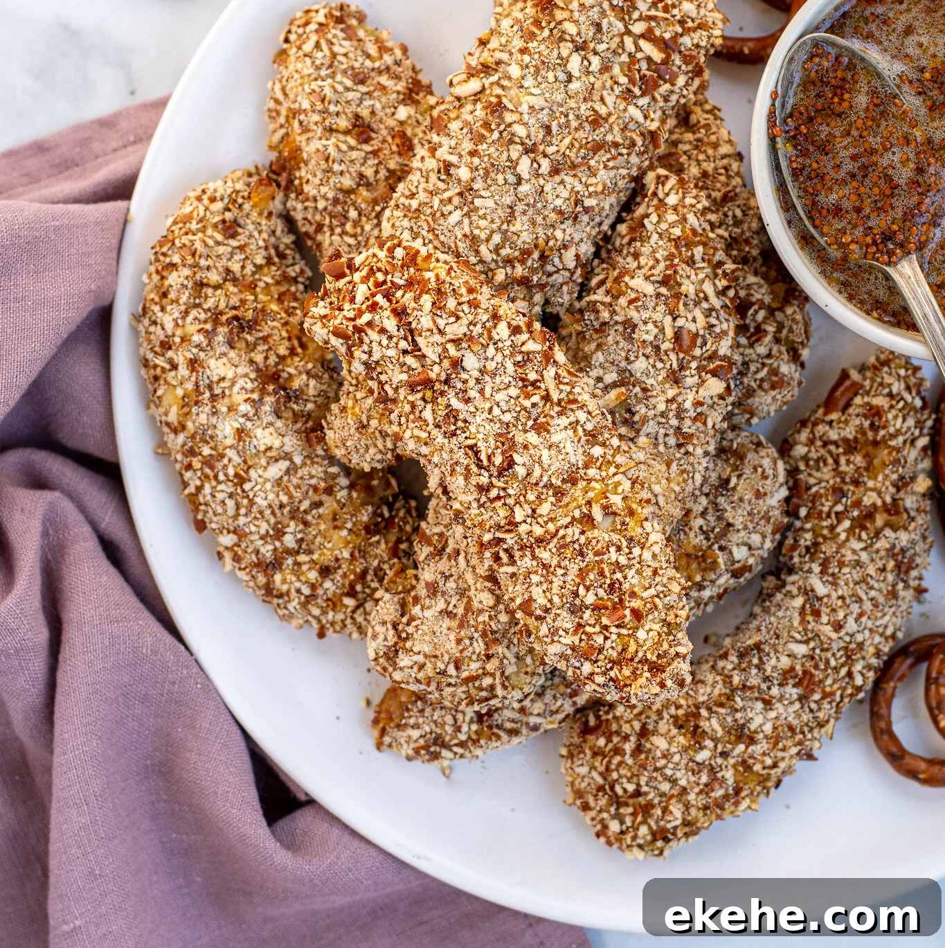 Plate full of a stack of Pretzel Crusted Chicken Tenders next to a small bowl of honey mustard.