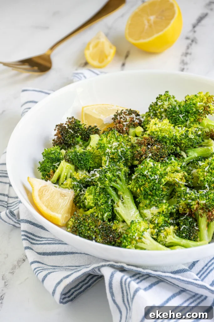 White bowl with cooked broccoli garnished with parmesan cheese and a lemon wedge.