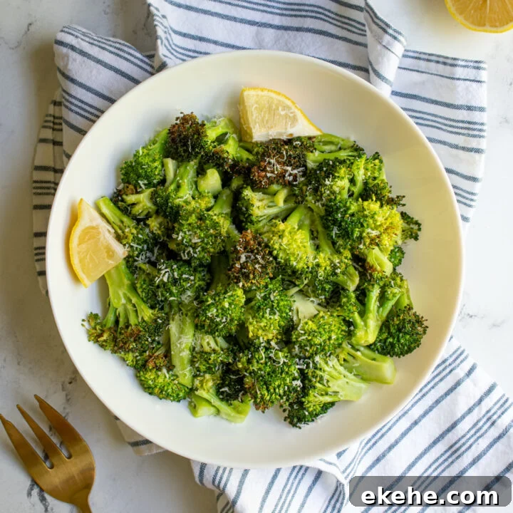 A white bowl on a blue striped towel filled with air fryer broccoli and garnished with lemon wedges.