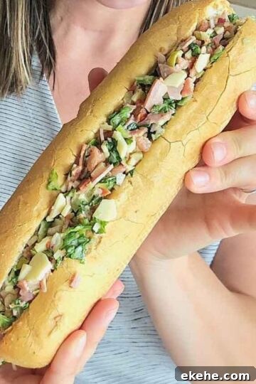 person holding a long sandwich stuffed with chopped meats and cheeses
